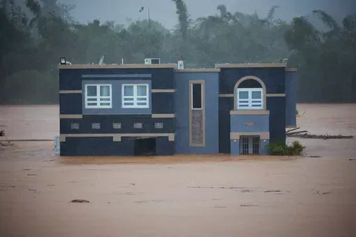 A home is submerged in floodwaters caused by Hurricane Fiona in Cayey, Puerto Rico, Sunday, Sept. 18, 2022.  According to authorities three people were inside the home and were reported to have been rescued.  (AP Photo/Stephanie Rojas)