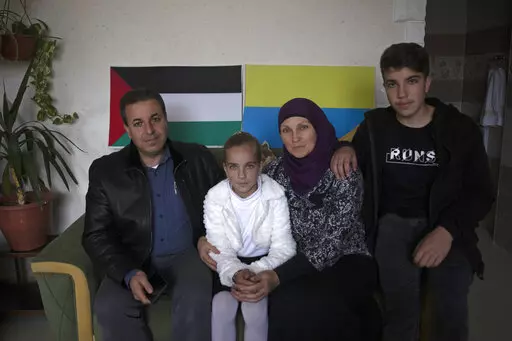Ukrainian Oksana al-Astal sits with her Palestinian husband and their children as they pose for a photo in front of representations of Palestinian and Ukrainian flags decorating the living room of their home in Khan Younis, southern Gaza Strip, Sunday, March 13, 2022. The al-Astal family is among dozens of Palestinian-Ukrainian families in the isolated territory who have experienced several wars firsthand — the most recent last May — and are now watching another unfold in Ukraine, where many