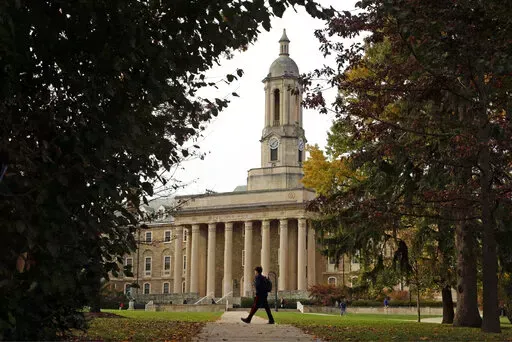 FILE- People walk by Old Main on the Penn State University main campus on Nov. 9, 2017 in State College, Pa. Applying to college is rarely easy, but applicants in 2022 are faced with one additional challenge: creating a compelling college application after nearly two years of disruptions as a result of the pandemic.   (AP Photo/Gene J. Puskar, File)