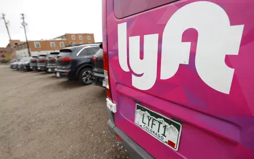 In this April 30, 2020, file photo, Kia Neros that are part of the Lyft ride-hailing fleet sit unused in a lot near Empower Field at Mile High in Denver.  Lyft says it’s adding a fuel surcharge of 55 cents to each ride its drivers perform to help offset recent gasoline price increases. The company said in a blog post on Wednesday, March 16, 2022, that the surcharge will be effective beginning next week, with all of the money going directly from riders to its drivers. (AP Photo/David Zalubowski