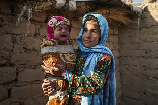 Qandi Gul holds her brother outside their home housing those displaced by war and drought near Herat, Afghanistan. Dec. 16, 2021. Gul’s father sold her into marriage without telling his wife, taking a down-payment so he could feed his family of five children. Without that money, he told her, they would all starve. He had to sacrifice one to save the rest. (AP Photo/Mstyslav Chernov)