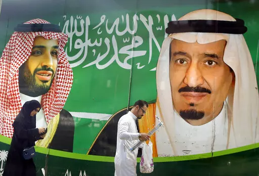 People walk past a banner showing Saudi King Salman, right, and his Crown Prince Mohammed bin Salman, outside a mall in Jiddah, Saudi Arabia, Saturday, March 7, 2020. A spike in global energy prices caused by Russia's war on Ukraine benefits Saudi Arabia as the world's top oil exporter, but problems remain for the kingdom's impulsive crown prince. (AP Photo/Amr Nabil, File)
