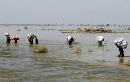 Victims of heavy flooding from monsoon rains crowd carry relief aid through flood water in the Qambar Shahdadkot district of Sindh Province, Pakistan, Sept. 9, 2022. The United Nations says weather disasters costing $200 million a day and irreversible climate catastrophe looming show the world is “heading in the wrong direction.” (AP Photo/Fareed Khan, File)