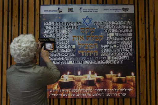 A woman photographs a poster in memory of members of the Zionist youth movement underground in Hungary during the Holocaust at a ceremony awarding the Jewish Rescuers Citation, at Kibbutz HaZorea, northern Israel, Tuesday, Dec. 13, 2022. Just before Nazi Germany invaded Hungary in March 1944, Jewish youth leaders in the eastern European country jumped into action: they formed an underground network that in the coming months would rescue tens of thousands of fellow Jews from the gas chambers. (AP