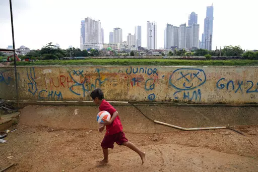 A young boy plays as high rise buildings at the main business district are seen in the background, in Jakarta, Indonesia, Tuesday, Jan. 25, 2022. Indonesian parliament last week passed the state capital bill into law, giving green light to President Joko Widodo to start a $34 billion construction project this year to move the country's capital from the traffic-clogged, polluted and rapidly sinking Jakarta on the main island of Java to jungle-clad Borneo island amid public skepticism. (AP Photo/D