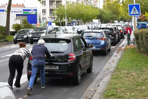 People push their car in a line of vehicles waiting to reach a station, Friday, Oct. 14, 2022 in Nanterre, outside Paris. Strikes in the French refineries of TotalEnergies group were still going on Friday, heavily disrupting fuel supplies as hard-left CGT union rejected a deal over pay rise that has been found between the energy giant and two other more moderate unions. (AP Photo/Michel Euler)