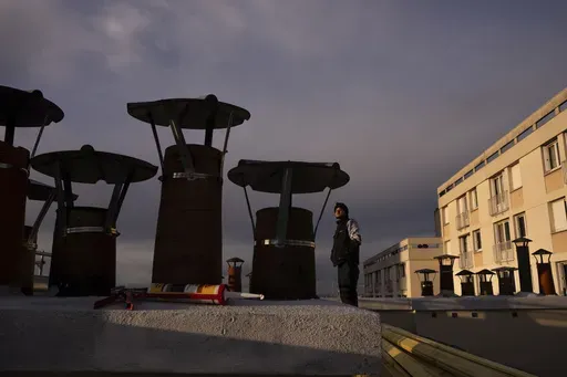 A roofer watches the sunset from the roof of a building in Paris, Wednesday, Nov. 20, 2024. (AP Photo/Louise Delmotte)