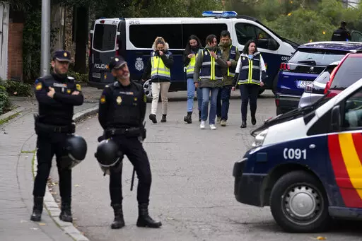 Police officers stand guard as other officers in yellow vests walk back at the cordoned off area next to the Ukrainian embassy in Madrid, Spain, Wednesday, Nov. 30, 2022. Spain's Interior Ministry says police are investigating reports of a blast at the Ukrainian embassy in Madrid. The ministry says police were told an employee at the embassy was slightly injured handling a letter in what it described as "a deflagration." (AP Photo/Paul White)