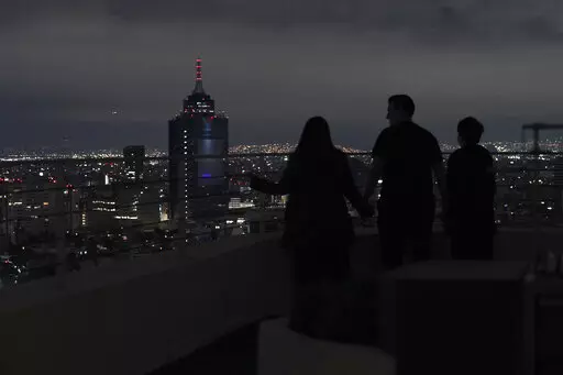 A family looks out at Mexico City from their apartment building rooftop after an earthquake early Thursday, Sept. 22, 2022. The magnitude 6.8 quake struck at 1:19 a.m. local time, causing at least two deaths, damaging buildings and setting off landslides near the epicenter in the western state of Michoacan. (AP Photo/Marco Ugarte)