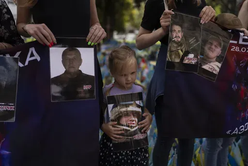 A girl holds a photo of a Ukrainian POW killed in the 2022 explosions at the Russian-controlled prison barracks in Olenivka, eastern Ukraine, during a memorial in Kyiv on July 29, 2023. An AP investigation interviewed survivors, family and investigators and obtained an internal U.N. analysis. All pointed to Russia as the culprit. (AP Photo/Jae C. Hong, File)