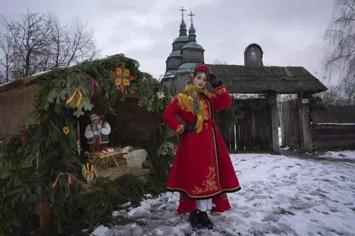 A woman dressed in national costume stands near the nativity scene to celebrate Christmas in the village of Pirogovo, outside the capital Kyiv, Ukraine, Monday, Dec. 25, 2023. (AP Photo/Efrem Lukatsky)