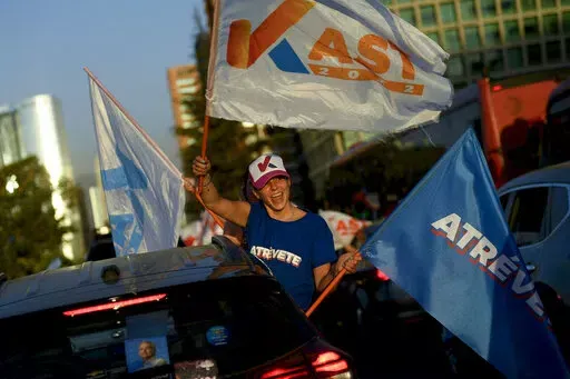 A follower of Chile's presidential candidate Jose Antonio Kast from the Partido Republicano, holds campaign flags during a rally in Santiago, Chile, Wednesday, Dec. 15, 2021. Chile votes in the runoff election on Dec. 19. (AP PhotoMatias Delacroix)