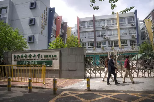 People walk past the gates of a closed primary school in Beijing, Thursday, April 28, 2022. While the U.S. and other countries are dropping restrictions and opening - with some health officials even saying the worst is over - China is keeping its international borders largely shut and closing off entire cities with millions of residents to all but essential travel. For the Chinese capital, however, the political stakes are heightened as the ruling party moves toward a crucial national congress. 