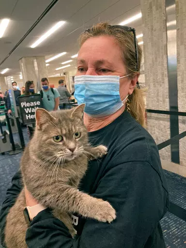 In this photo provided by Janet Williams, "Ashes" the cat, who had been lost by a Maine family since 2015, is held by Williams at Tampa International Airport, Wednesday Feb. 9, 2022, in Tampa, Fla. Denise Cilley, of Chesterville, Maine, says she was shocked to get a voicemail last week announcing her cat, Ashes, had been found nearly 1,500 miles away in Florida. Ashes is being returned to Maine on Wednesday, with Cilley planning to be on hand to collect her pet at Portland International Jetport.