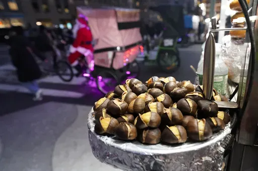 Chestnuts are displayed at a food vendor as a person dressed as Santa Claus offers rides, Thursday, Dec. 12, 2024, in New York. (AP Photo/Alyssa Goodman)
