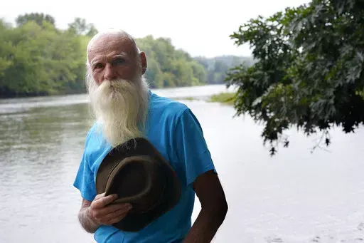 FILE — David Lidstone, 81, stands for a photograph near the Merrimack River, Tuesday, Aug. 10, 2021, in Boscawen, N.H. Lidstone, a former hermit in New Hampshire, known to locals as "River Dave," whose cabin in the woods burned down after nearly three decades on the property that he was ordered to leave, and who received more than $200,000 in donations, has been charged with trespassing there once again. Lidstone still disputes that he is on the property, and was arrested on a trespassing char