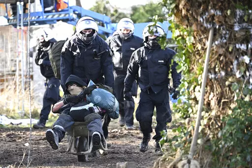 Police officers push a climate activist with a wheelbarrow off the site in the village Luetzerath in Erkelenz, Germany, Sunday, Jan. 15, 2023. The energy company RWE wants to excavate the coal lying under Luetzerath, for this purpose, the hamlet on the territory of the city of Erkelenz at the opencast lignite mine Garzweiler II is to be demolished. (Federico Gambarini/dpa via AP)