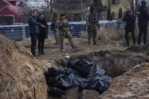 People stand next to a mass grave in Bucha, on the outskirts of Kyiv, Ukraine, April 4, 2022. AP journalists saw dozens of bodies in Bucha, many of them shot at close range, and some with their hands tied behind them. (AP Photo/Rodrigo Abd, File)