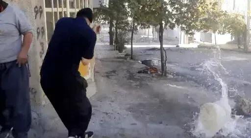 In this image from video provided by Hengaw Organization for Human Rights, a protester reacts after a water container was hit by a bullet during a protest in Javanroud, a Kurdish town in western Iran, Monday, Nov. 21, 2022. (Hengaw Organization for Human Rights via AP)
