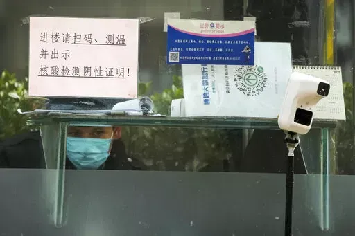 A security guard keeps watch inside a booth displaying a temperature scan device and a travel QR code, outside an office building in Beijing, Monday, Dec. 12, 2022. China will drop a travel tracing requirement as part of an uncertain exit from its strict "zero-COVID" policies that have elicited widespread dissatisfaction. (AP Photo/Andy Wong)