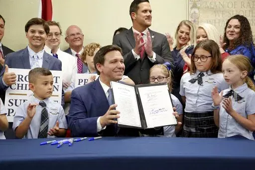 Florida Gov. Ron DeSantis displays the signed Parental Rights in Education, aka the Don't Say Gay bill, flanked by elementary school students during a news conference on Monday, March 28, 2022, at Classical Preparatory school in Shady Hills. (Douglas R. Clifford/Tampa Bay Times via AP)