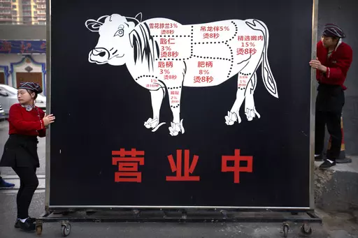 Restaurant workers move a sign advertising the grand opening of a beef hotpot restaurant along a street in Beijing, Thursday, Oct. 12, 2017. As incomes in China have risen in the last decade, beef, once a luxury, is now popular on middle-class menus. (AP Photo/Mark Schiefelbein, File)