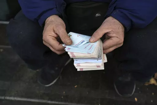 A street money exchanger poses for a photo without showing his face as he counts Iranian banknotes at a commercial district in downtown Tehran, Iran, Friday, Dec. 23, 2022. Iran’s currency fell to a record low on Sunday, plunging to 613,500 to the dollar, as its people celebrated the Persian New Year. (AP Photo/Vahid Salemi, File)