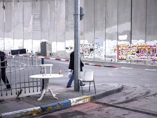 Palestinians walk by a section of the Israeli separation barrier in the West Bank village of Abu Dis in the outskirts of Jerusalem, Monday, Jan. 31, 2022. Twenty years after Israel decided to built its controversial separation barrier amid a wave of Palestinian attacks, it remains in place, even as Israel encourages its own citizens to settle on both sides and admits tens of thousands of Palestinian laborers. (AP Photo/Oded Balilty)