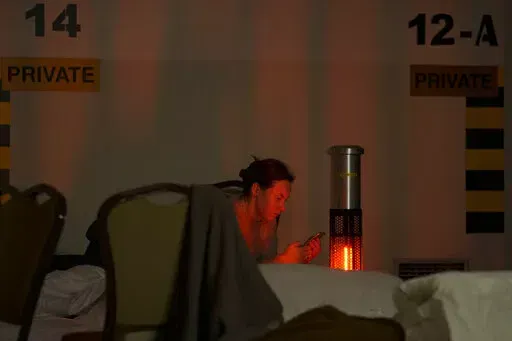 A woman looks at her mobile phone in a hotel underground parking turned into a bomb shelter during an air raid alert in Kyiv, Ukraine, Sunday, Feb. 27, 2022. Terrified men, women and children sought safety inside and underground, and the government maintained a 39-hour curfew to keep people off the streets as more than 150,000 Ukrainians fled to neighboring countries and the United Nations warned the number could grow to 4 million if fighting escalates.(AP Photo/Vadim Ghirda)