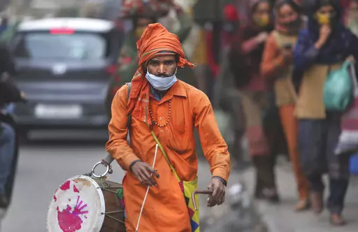 A man wears his face mask below his nose and walks in a market area with a traditional percussion instrument in Jammu, India, Saturday, Jan.15, 2022. It’s mandatory to wear a mask in India. And police are out on the streets, watching people to make sure they are in place. People caught without wearing a mask are fined. Some local governments, like the one in the capital New Delhi, have recruited new staff to ensure the rules are followed.c(AP Photo/Channi Anand)