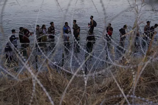 Migrants wait to climb over concertina wire after they crossed the Rio Grande and entered the U.S. from Mexico, Sept. 23, 2023, in Eagle Pass, Texas. A divided Supreme Court on Tuesday, March 19, 2024, lifted a stay on a Texas law that gives police broad powers to arrest migrants suspected of crossing the border illegally, while a legal battle over immigration authority plays out. (AP Photo/Eric Gay, File)