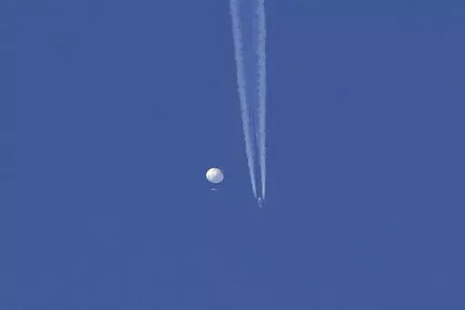 In this photo provided by Brian Branch, a large balloon drifts above the Kingstown, N.C. area, with an airplane and its contrail seen below it. The United States says it is a Chinese spy balloon moving east over America at an altitude of about 60,000 feet (18,600 meters), but China insists the balloon is just an errant civilian airshipused mainly for meteorological research that went off course due to winds and has only limited “self-steering” capabilities. (Brian Branch via AP)