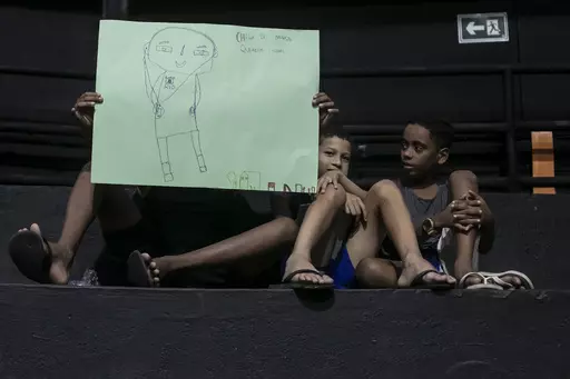 Children hold drawings that represent their experiences of living in the Mare favela at an event to launch the book titled “I was supposed to be at school” in the Mare favela of Rio de Janeiro, Brazil, Monday, March 25, 2024. Dozens of kids and teenagers from one of Rio de Janeiro's most violent favelas gathered on Monday to celebrate their most important piece of work yet: a book that aims to show authorities how they see police violence in their Maré community from a young age. (AP Photo/