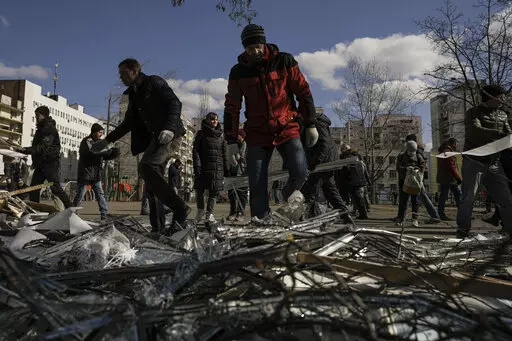 People clear debris outside a medical center damaged after parts of a Russian missile, shot down by Ukrainian air defense, landed on a nearby apartment block, according to authorities, in Kyiv, Ukraine, Thursday, March 17, 2022. Russian forces destroyed a theater in Mariupol where hundreds of people were sheltering Wednesday and rained fire on other cities, Ukrainian authorities said, even as the two sides projected optimism over efforts to negotiate an end to the fighting. (AP Photo/Vadim Ghird