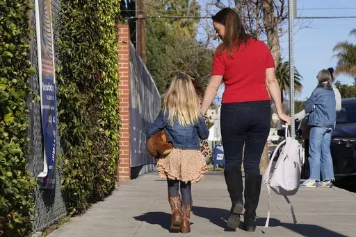 Kelli Ferrone walks her daughter into a temporary school Friday, Jan. 24, 2025, in Los Angeles, as they wait for Canyon Charter Elementary School to reopen after being impacted by smoke and ash from the Palisades Fire. (AP Photo/Brittany Peterson)