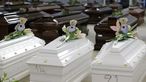 Teddy bears and flowers placed are placed on the coffins of deceased migrants inside a hangar at Lampedusa's airport, Italy, Saturday, Oct. 5, 2013. A decade ago this year, the head of the EU's executive branch, Jose Manuel Barroso stood visibly shaken before hundreds of coffins holding the corpses of migrants drowned off the Italian Island of Lampedusa. (AP Photo/Luca Bruno, File)