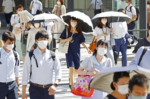 People, some of them holding parasols, cross an intersection amid heat, in Tokyo, Monday, June 27, 2022.  Japan’s government issued a warning for possible power crunch in the Tokyo area Monday, asking offices and residents to save energy as the capital region is hit by sweltering heat, with weather officials announcing an earliest end to the rainy season in decades. (Yusuke Ogata/Kyodo News via AP)