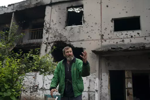 Viacheslav Myronenko, 71, stands in front of the entrance of a damaged building where he lives in the freed village of Hrakove, Ukraine, Tuesday, Sept. 13, 2022. Myronenko has been living in the basement of his bombed-out apartment building with three neighbors for more than four months. (AP Photo/Leo Correa)