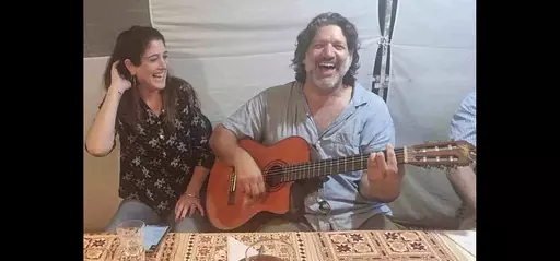 This image provided by Eran Shani shows Shlomi Mathias playing the guitar as his wife, Debbie ‘Shahar’ Mathias, laughs and sings next to him at her 50th birthday party on Oct. 1, 2023, in Lehavim, Israel. They both died days later while protecting their 16-year-old son, Rotem Mathias, from Hamas fighters who attacked their kibbutz in Israel near the border with Gaza on Oct. 7, 2023. (Eran Shani via AP)