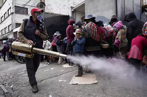 A worker sprays disinfectant around people who traveled from the provinces to Monte de Oración church for donated food and clothing during the church's annual Good Samaritan campaign in La Paz, Bolivia, Tuesday, Dec. 28, 2021. Due to the COVID-19 pandemic, the church is distributing the goods outdoors. (AP Photo/Freddy Barragan)