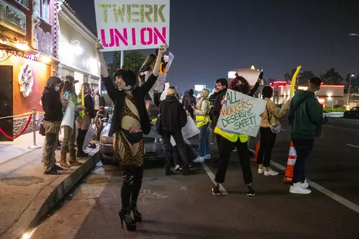 A protester identified as "Reagan" holds a sign outside the Star Garden Topless Dive Bar on Saturday, March 26, 2022 in the North Hollywood area of Los Angeles. Dancers at the bar, who have for 15 months been seeking safer workplace conditions, better pay and health insurance, among other benefits, are poised to become the only unionized group of strippers in the U.S. (Francine Orr/Los Angeles Times via AP)