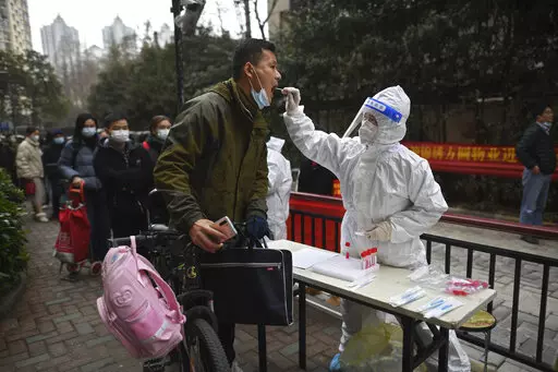 A man holding his bicycle with a school bag on it gets a throat swab during a mass COVID-19 test at a residential compound in Wuhan in central China's Hubei province, Tuesday, Feb. 22, 2022. Wuhan, the first major outbreak of the coronavirus pandemic has reported more than dozen new coronavirus cases this week, prompting the authority to step up precautious measures. (Chinatopix via AP)