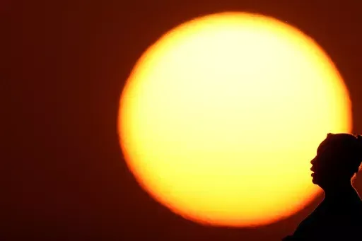 A woman is silhouetted against the setting sun as triple-digit heat indexes continue in the Midwest, Aug. 20, 2023, in Kansas City, Mo. The rate Earth is warming hit an all-time high in 2023 with 92% of last year’s surprising record-shattering heat caused by humans, top scientists calculated. (AP Photo/Charlie Riedel, File)