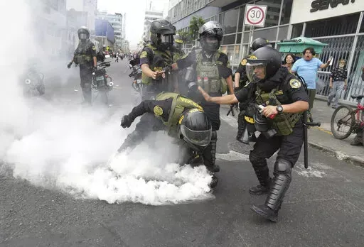 Police officers pick up a tear gas canister that was thrown back at them by anti-government protesters who traveled to the capital from across the country to march against Peruvian President Dina Boluarte in Lima, Peru, Wednesday, Jan. 18, 2023. Protesters are seeking immediate elections, Boluarte's resignation, the release of ousted President Pedro Castillo and justice for the dozens of protesters killed in clashes with police. (AP Photo/Martin Mejia)