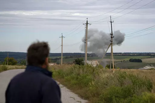 Viktor Lubinets, an agronomist at the Veres farm, looks at smoke rising in the air following a explosion in Novomykolaivka, eastern Ukraine, Saturday, Sept. 10, 2022. Returning to sowing and harvesting "will be difficult, very difficult," said Lubinets, an agronomist at the Veres farm. Even if the fighting ends, the fields must be cleared of unexploded ordinance and shrapnel before they can be worked. (AP Photo/Leo Correa)