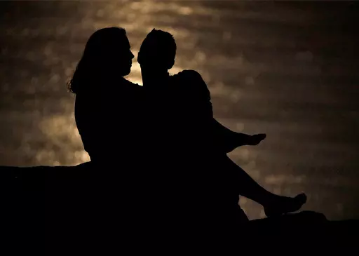 In this June 27, 2018, file photo a couple is silhouetted against moonlight reflecting off the Missouri River as they watch the full moon rise beyond downtown buildings in Kansas City, Mo. Money can create stress within a relationship, but talking through expectations and money beliefs can help couples get on the same page. In fact, conflict over money can be healthy, partly because we often partner with people who are our financial opposites. (AP Photo/Charlie Riedel, File)