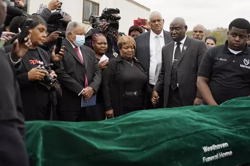 Surrounded by family members and holding hands with civil rights attorney Ben Crump, center right, Bettersten Wade, center, mother of Dexter Wade, a 37-year-old man who died after being hit by a Jackson, Miss., police SUV driven by an off-duty officer, watches her son's body transferred to a mortuary transport in Raymond, Miss. Nov. 13, 2023. An independent pathologist says the deceased Mississippi man had a wallet in the front pocket of the jeans he was buried in that contained his home address
