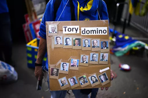 A protester holds a placard with photographs of British Prime Minister Boris Johnson, bottom right, his government cabinet members and Russia President Vladimir Putin, top left, outside the Houses of Parliament, in London, Wednesday, July 6, 2022. A defiant British Prime Minister Boris Johnson is battling to stay in power after his government was rocked by the resignation of two top ministers. His first challenge is getting through Wednesday, where he faces tough questions at the weekly Prime Mi