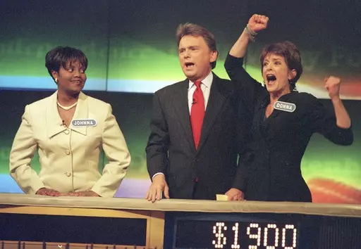 Johnna Goodwin, left, watches as Donna Handel, right, reacts after winning on "Wheel of Fortune," with host Pat Sajak during a taping of the game show in Philadelphia on April 17, 1999. The game show was in Philadelphia for the weekend taping a week's worth of shows. Ryan Seacrest will replace the retiring Sajak as host of “Wheel of Fortune.” (AP Photo/William Thomas Cain, File)
