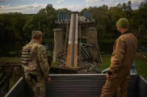 Ukrainian soldiers remove metal structure pieces as they work on a bridge damaged during fighting with Russian troops in Izium, Ukraine, Monday, Oct. 3, 2022. A series of embarrassing military losses for Moscow in recent weeks has presented a growing challenge for prominent hosts of Russian news and political talk shows scrambling to find ways to paint Kyiv's gains in a way that is still favorable to the Kremlin. (AP Photo/Francisco Seco)